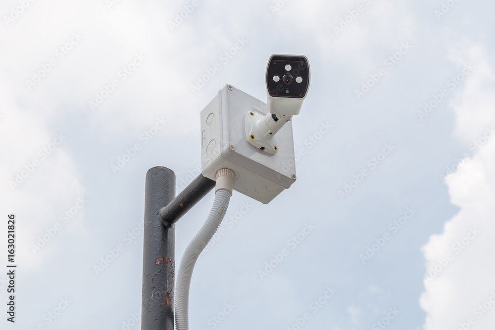 Security camera, CCTV is installed for monitoring on building with blurred blue sky in background Security camera, CCTV is installed for monitoring on building with blurred blue sky in background