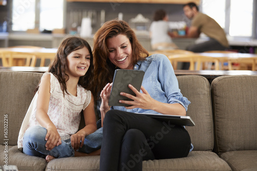 Mother And Daughter Sitting On Lounge Sofa Using Digital Devices