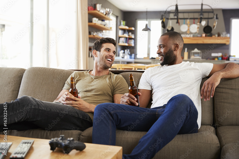 Two Male Friends Sit On Sofa And Watch Sports On Television Two Male Friends Sit On Sofa And Watch Sports On Television