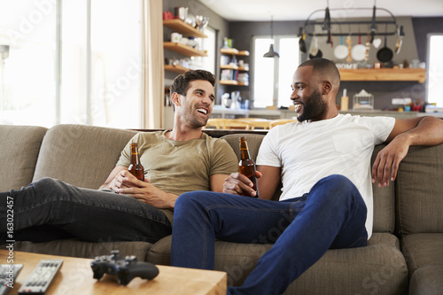 Two Male Friends Sit On Sofa And Watch Sports On Television