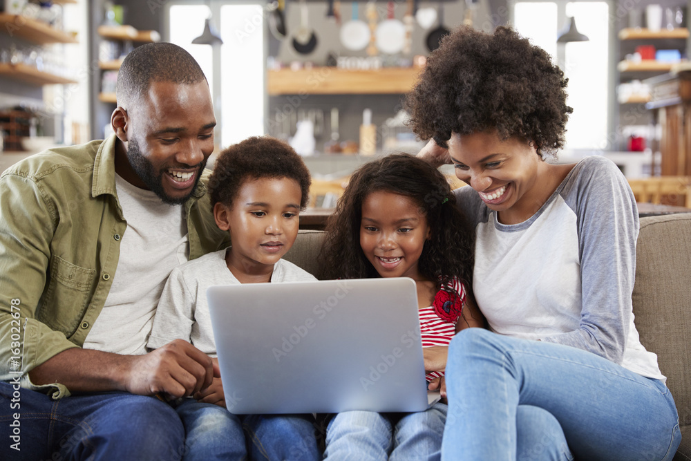 Family Sitting On Sofa In Open Plan Lounge Using Laptop Family Sitting On Sofa In Open Plan Lounge Using Laptop