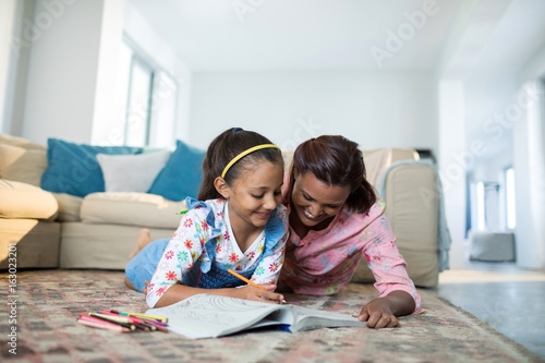 Mother assisting her daughter with drawing in living room