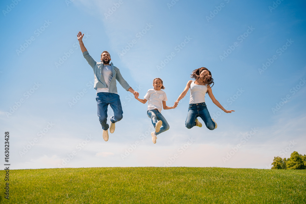 Happy young family with one child holding hands and jumping on meadow Happy young family with one child holding hands and jumping on meadow
