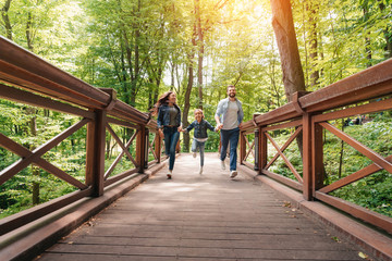 young happy interracial family running through the wooden bridge in sunny forest
