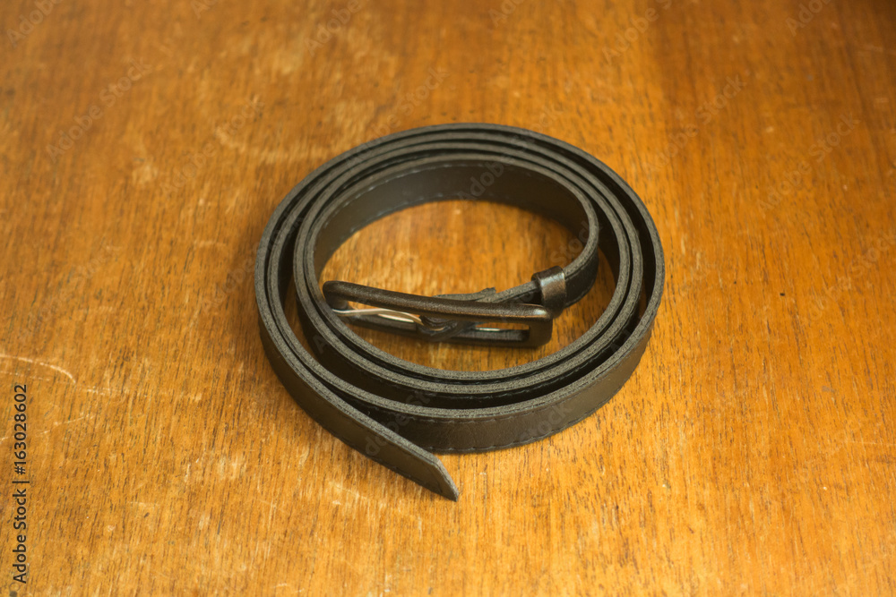 Black leather belt with a buckle on wooden table Black leather belt with a buckle on wooden table