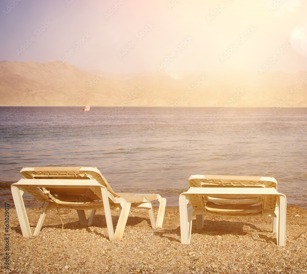 tropical sea beach and two chaise lounger at sunset light. Summer travel and vacation concept tropical sea beach and two chaise lounger at sunset light. Summer travel and vacation concept