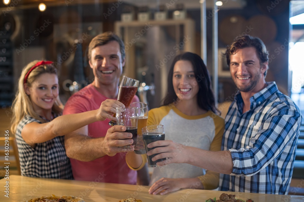 Portrait of happy friends toasting beer at table in bar