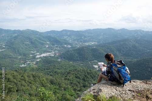 Young girl Hipster with backpack enjoying with smartphone on peak of foggy mountain. Tourist traveler on background view .Hiker in holiday trip in Thailand country.