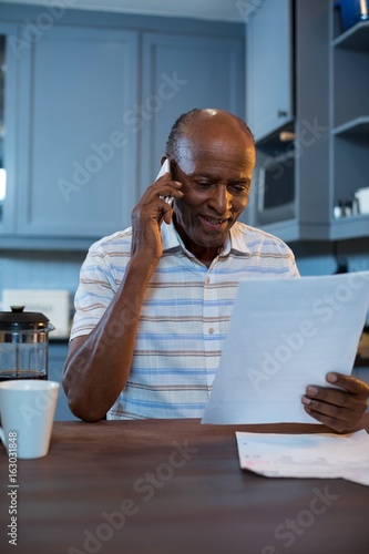 Smiling man reading document while using phone at home photo