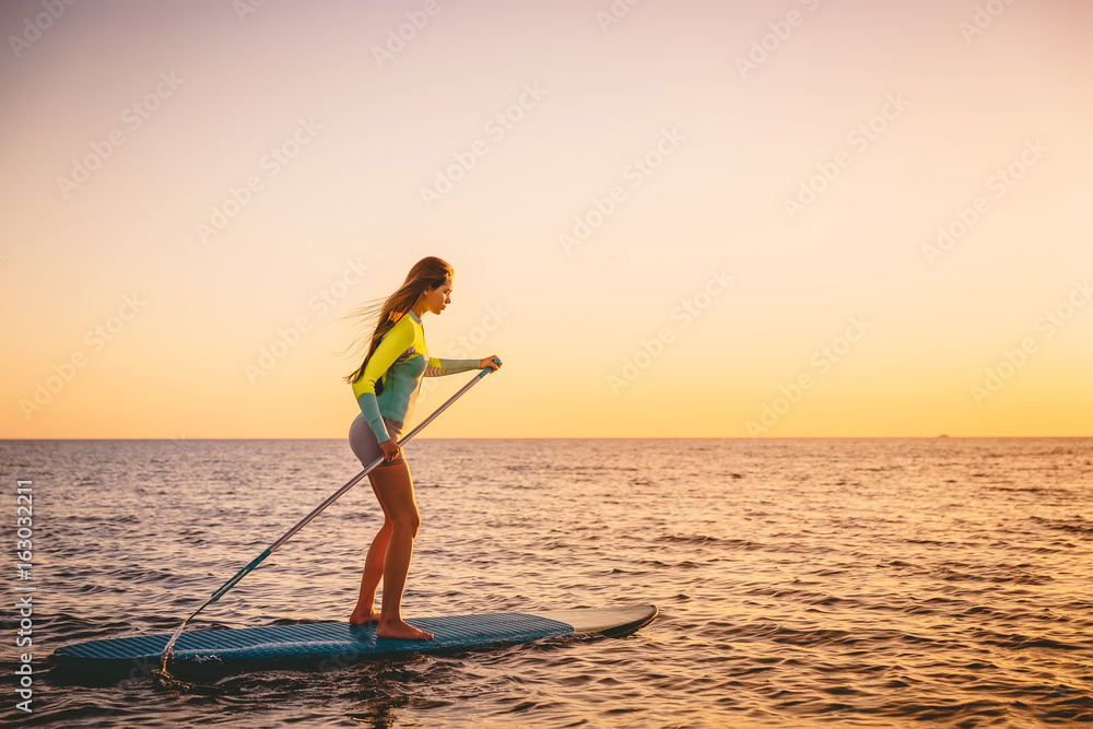 Sporty young woman stand up paddle surfing with beautiful sunset colors