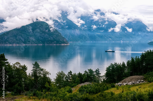 White ship on the background of mountains and forest covered with clouds .