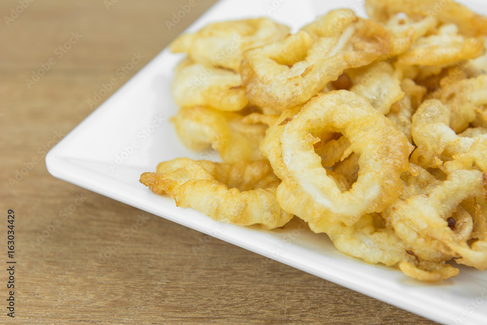 crispy deep fried squid ring in white plate on wooden surface, close up crispy deep fried squid ring in white plate on wooden surface, close up