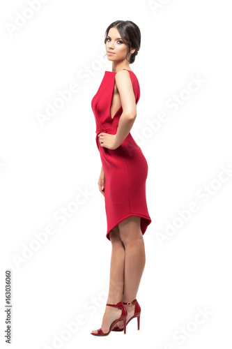 Side view of pretty young latin woman in red dress with hands on hips looking at camera.  Full body length portrait isolated on white background.  © sharplaninac