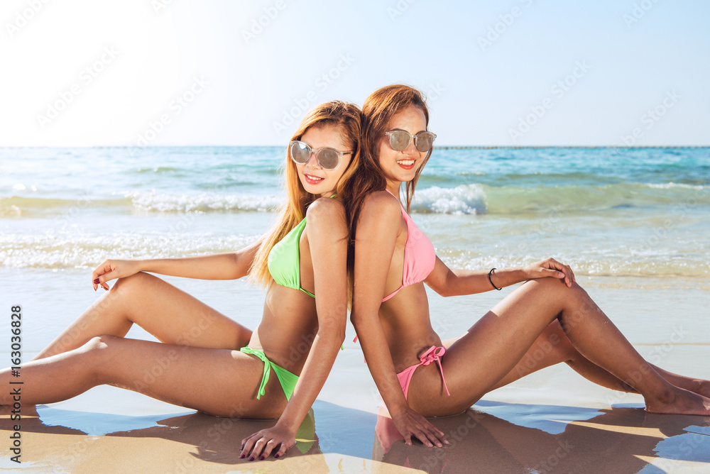 Two sexy women in bikinis on the sunny beach. Best friends having fun, Summer vacation holiday lifestyle. Happy women relaxing freedom on white sand.