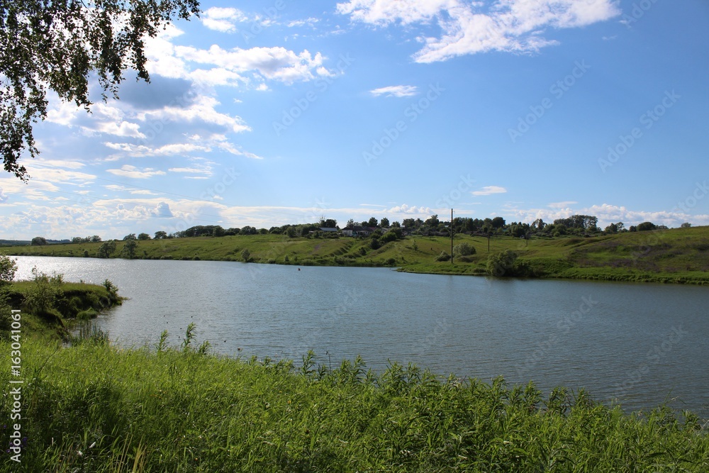 The lake is in good sunny weather. The water is riddled with a slight ripple. The shores of the lake are covered with luscious green vegetation. The lake is in good sunny weather. The water is riddled with a slight ripple. The shores of the lake are covered with luscious green vegetation.