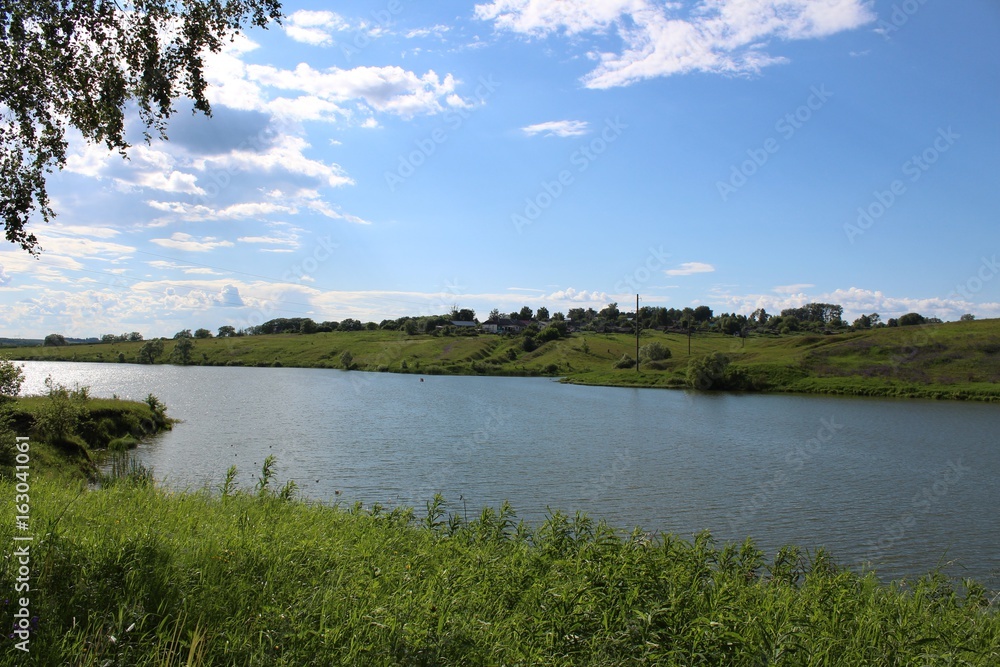 The lake is in good sunny weather. The water is riddled with a slight ripple. The shores of the lake are covered with luscious green vegetation.