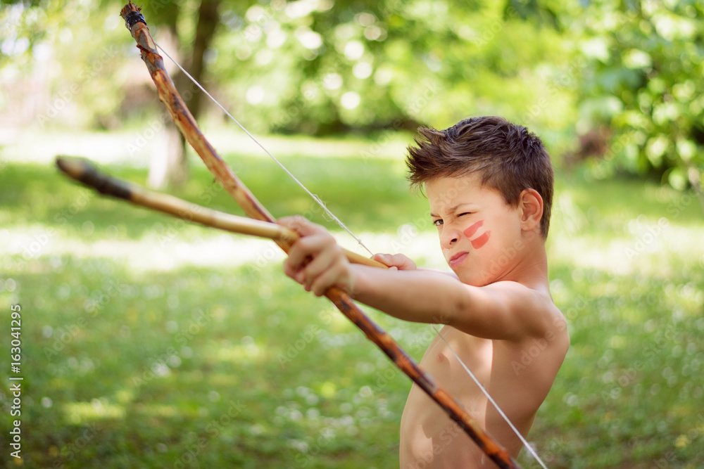 Adorable young boy playing native Indian with toy bow and arrow is ...