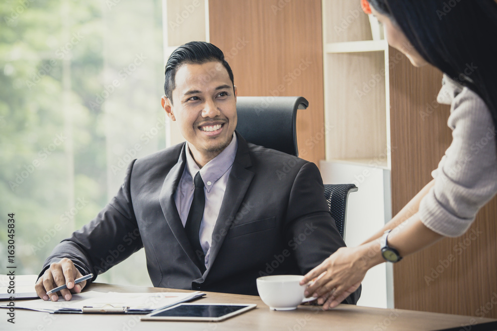 Asian businessman looking to secretary when give a coffee cup at working place, man with relax time concept. Asian businessman looking to secretary when give a coffee cup at working place, man with relax time concept.