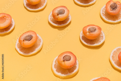 Juicy halves of apricots placed on sliced pieces of lemons on yellow background. Summer fruit