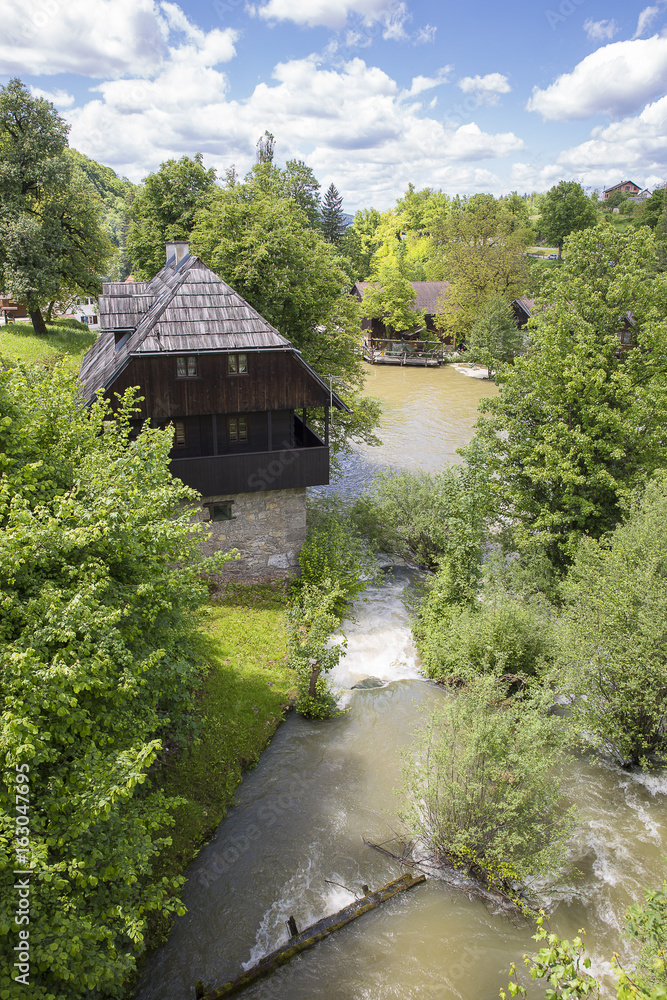 Croatian village of Rastoke by a river canyon with wooden houses in a green landscape with trees and a waterfall, Croatia