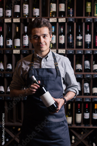 Canvastavla Portrait of a sommelier standing in a wine cellar holding a glass of wine and sh
