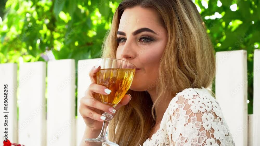 Beautiful blonde woman in white dress sitting in the restaurant and drinking cocktail closeup Beautiful blonde woman in white dress sitting in the restaurant and drinking cocktail closeup