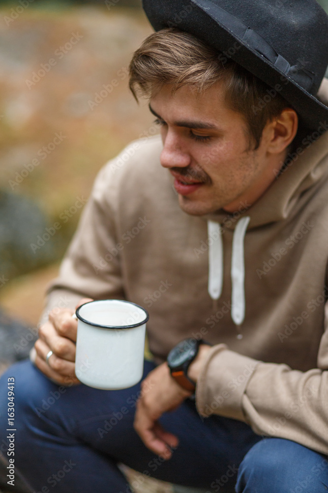 Portrait hiking man sits by firecamp near tent and drinks from mug Portrait hiking man sits by firecamp near tent and drinks from mug
