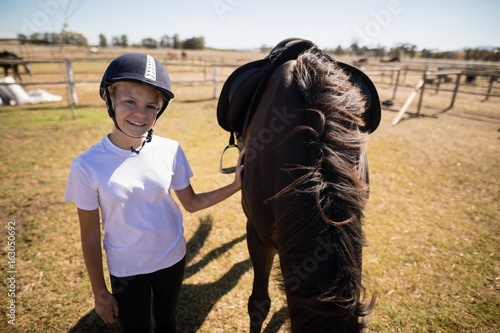 Smiling girl standing next to the brown horse in the ranch