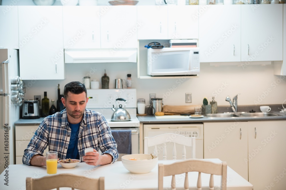 Man using mobile phone while having breakfast in kitchen Man using mobile phone while having breakfast in kitchen