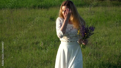 Beautiful young woman in white dress gathering flowers on the meadow slow motion