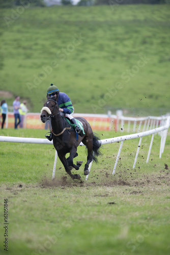 single race horse and jockey racing down the track kicking up dirt