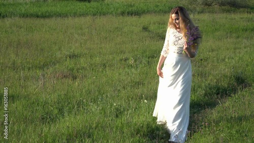 Beautiful young woman walking on the meadow with flowers