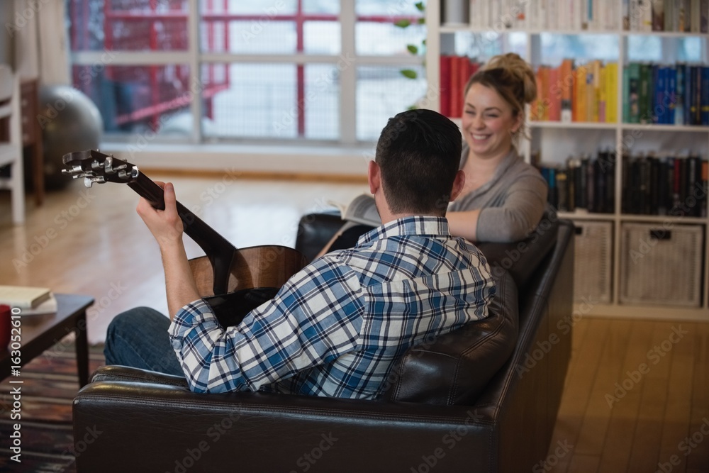 Man playing guitar while woman sitting beside him in living room Man playing guitar while woman sitting beside him in living room