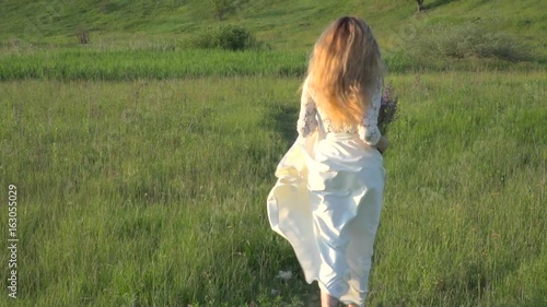 Beautiful blonde woman in white dress running on the meadow slow motion