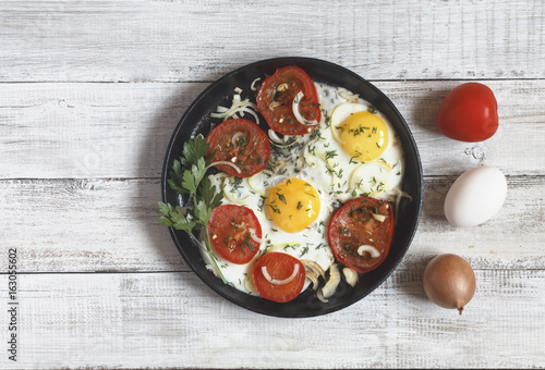 Fried eggs with vegetables and greens (tomatoes, onion, dill) on wooden background. Copy space.