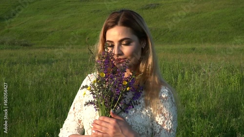 Beautiful woman in white dress with flowers smiling and looking to the camera on the meadow slow motion