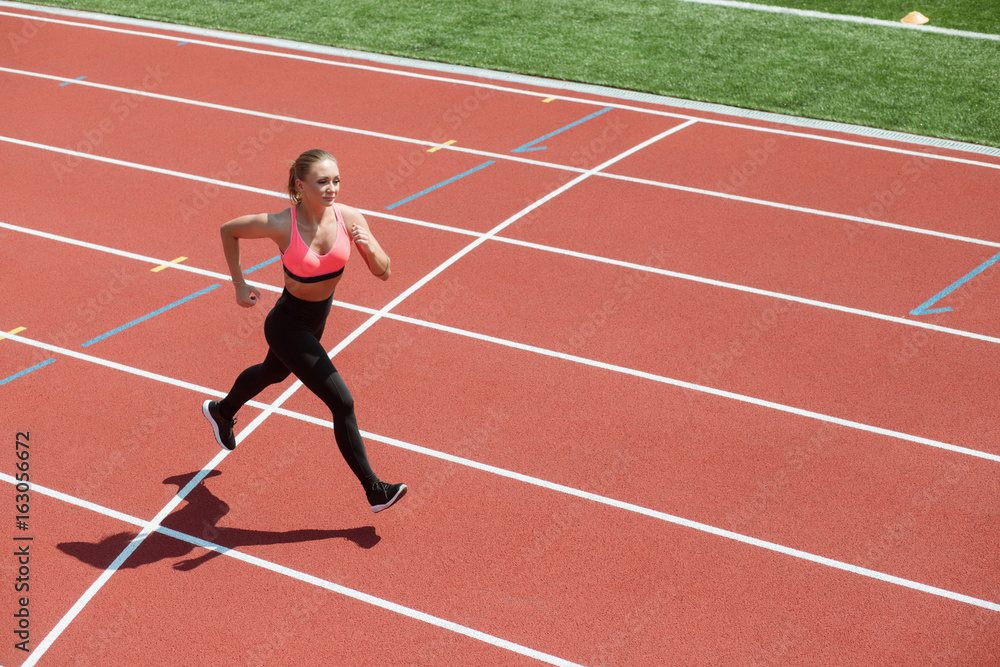 Young sport woman sprinter athlete running on stadium track