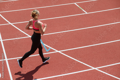 Young sport woman sprinter athlete jogging on stadium track, healthy lifestyle concept