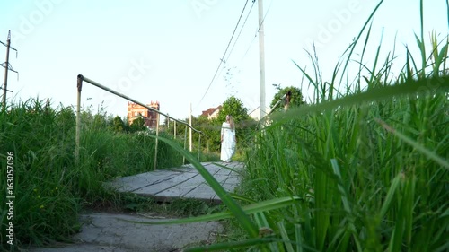 Young woman in the white dress crossing bridge on nature