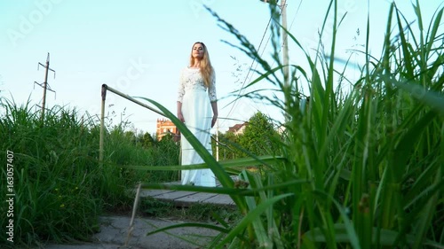 Young blonde woman in the white dress crossing bridge on nature