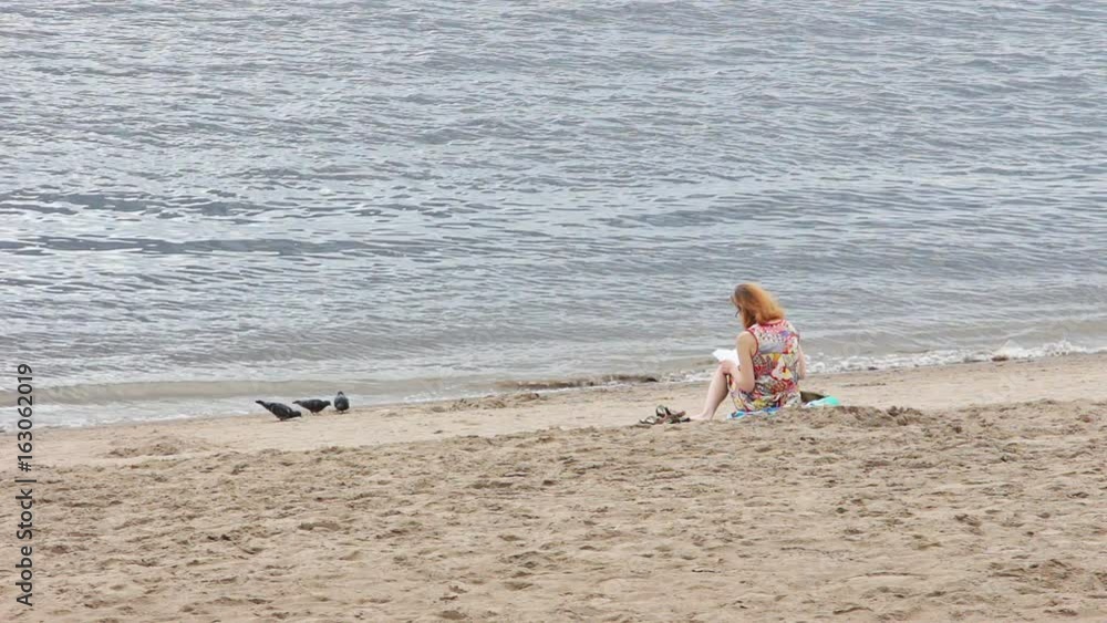 Lonely girl with red hair reading a book sitting on the beach Lonely girl with red hair reading a book sitting on the beach