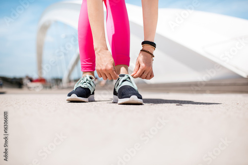 Woman lacing up a sports sneakers standing outdoors on the white bridge