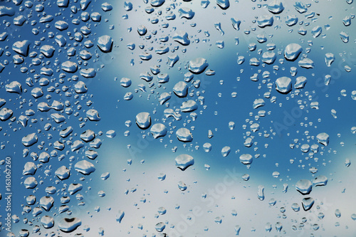 Rain drops on window glass with blue cloudy sky in background , spring rainy day