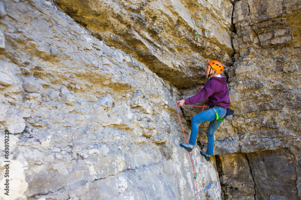 The woman in the helmet climbs the rock.