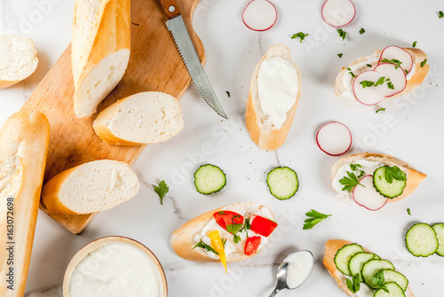 Healthy food. Spring, summer snacks. Sandwiches toast with homemade cream cheese and fresh vegetables - radish, cucumber, tomatoes, onion, pepper. On a white marble table. Top view