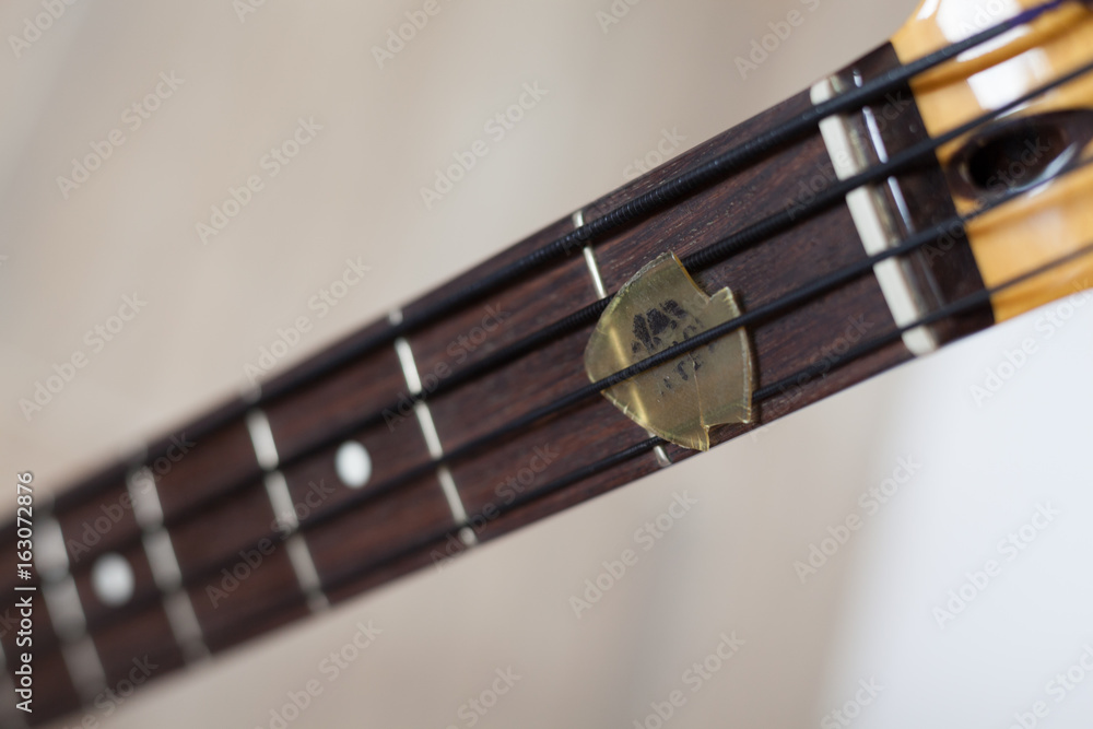 Bass guitar fingerboard closeup with a damaged pick stuck between black  nylon strings Stock Photo | Adobe Stock