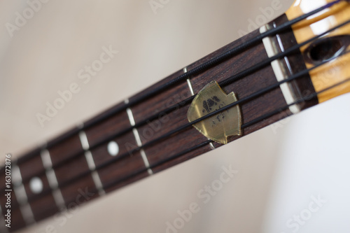 Bass guitar fingerboard closeup with a damaged pick stuck between black nylon strings