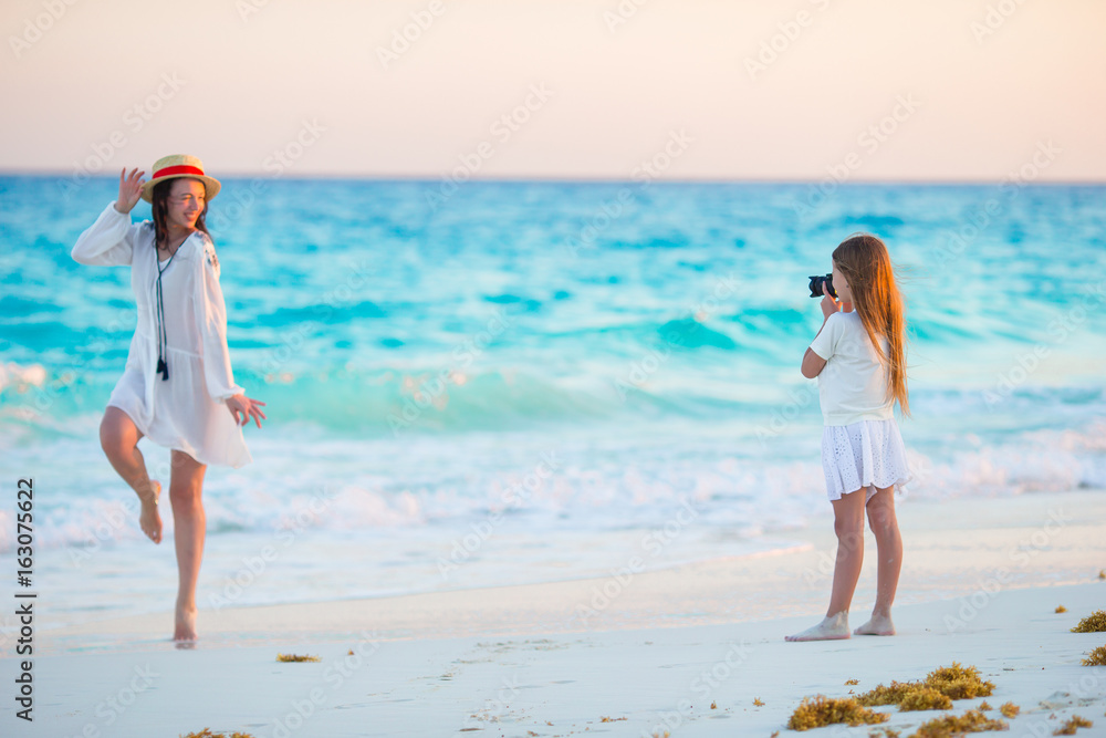 Little girl taking photo of young mother at tropical beach at sunset
