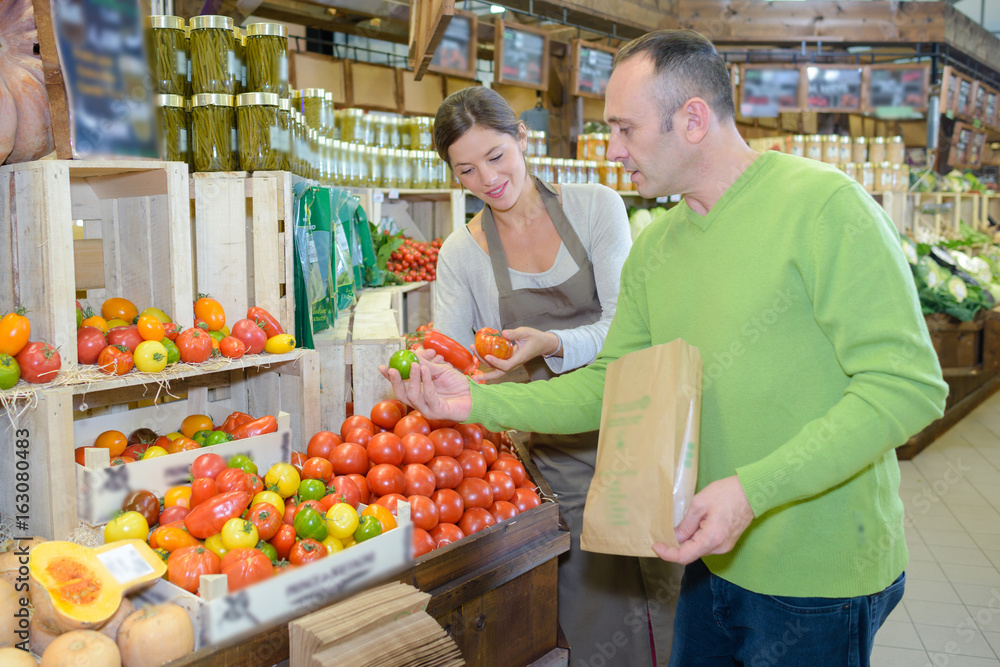shop assistant helping man to choose fruits and vegetables