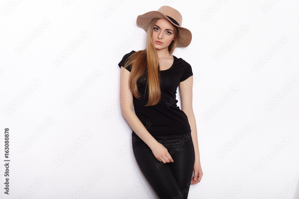 Young beautiful fashion model in women black t-shirt trendy hat black torn jeans posing in studio against white background Young beautiful fashion model in women black t-shirt trendy hat black torn jeans posing in studio against white background